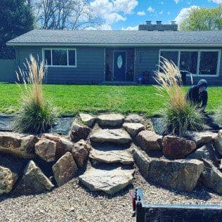 Person landscaping a stone steps garden with ornamental grasses in front of a house.